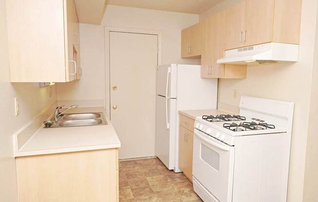 A gallery-style kitchen with a stove, sink, and refrigerator at Madeira Apartments in Kalamazoo, MI