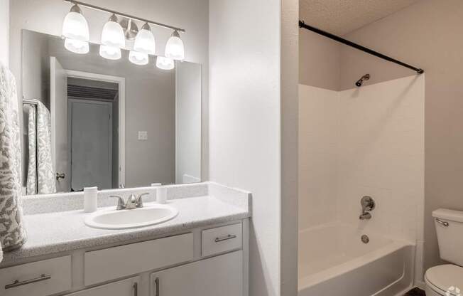 A white bathroom with a sink, mirror, and bathtub.