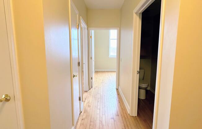 a hallway with a wood floor and a door to a bathroom