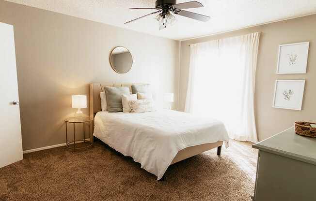 A bedroom with a bed, a ceiling fan, and a carpeted floor.