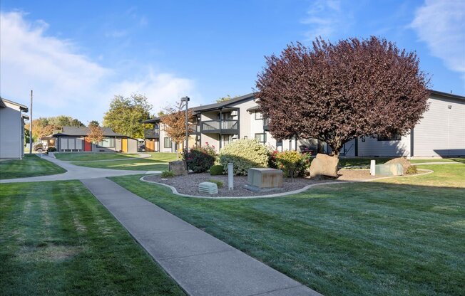 Side walk entering the community through green grass and large trees. Apartment buildings in the background. at Brix, Washington, 99362