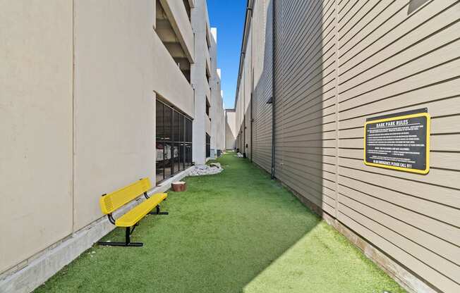 A yellow bench sits on a green lawn next to a building.