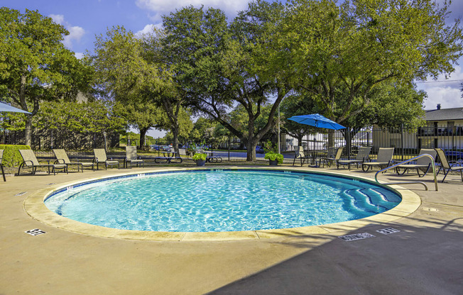 our resort style swimming pool is surrounded by lounge chairs and trees