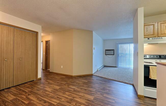 an empty living room and kitchen with wood flooring and a door to the bedroom. Fargo, ND Flagstone Apartments
