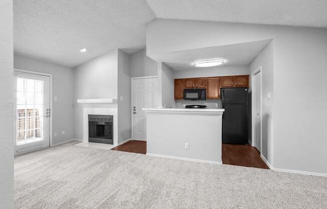 A spacious living room with a fireplace and a kitchenette in the background.