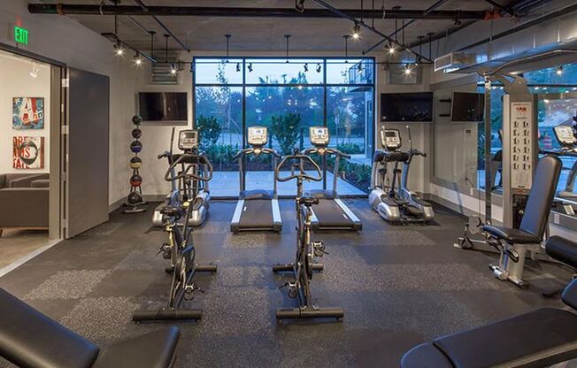 a gym with cardio equipment and a large window