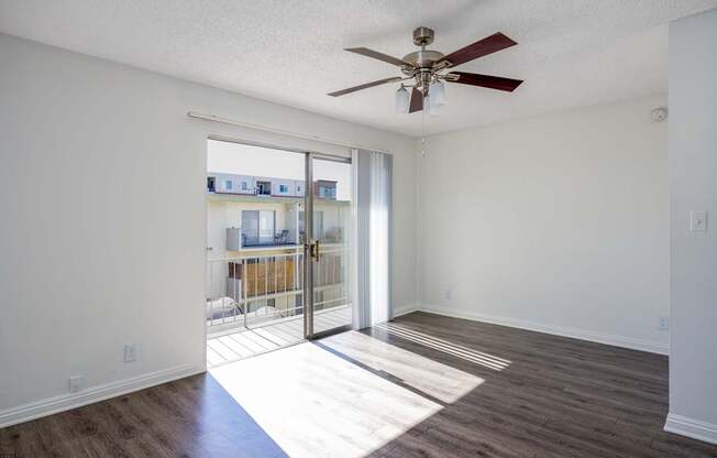 an empty living room with a ceiling fan and sliding glass doors to a balcony