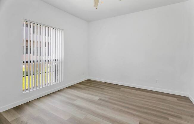 A room with a window covered by white blinds and wooden flooring.