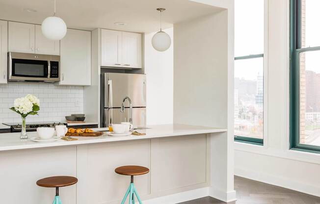 A kitchen with a white counter and two blue stools at The Pennsylvanian Apartments, Pittsburgh, Pennsylvania