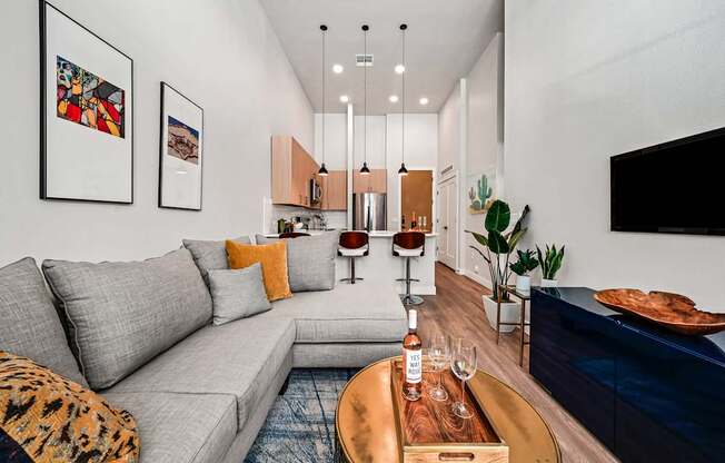 A modern living room with a grey sofa, a wooden coffee table, and a TV on the wall.