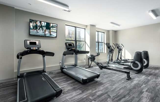 a gym with various cardio machines and a tv on the wall