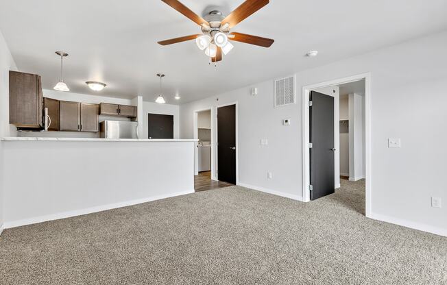 a living room with a ceiling fan and a kitchen in the background