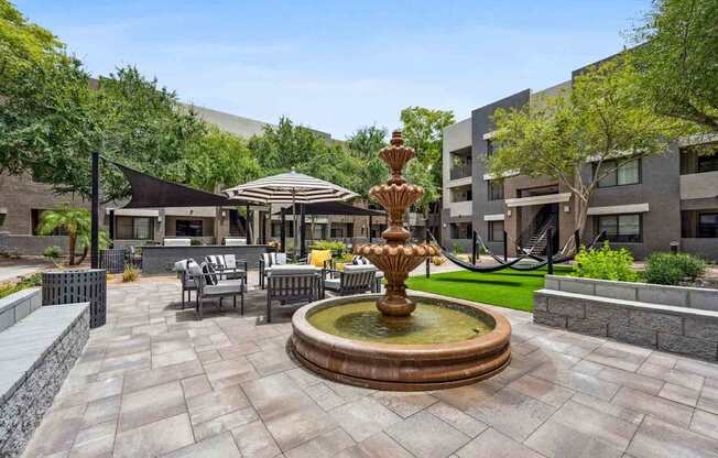 A fountain in the middle of a courtyard surrounded by chairs and umbrellas.