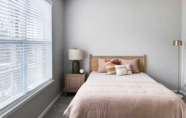 A bedroom with a bed, nightstand, and window with blinds.