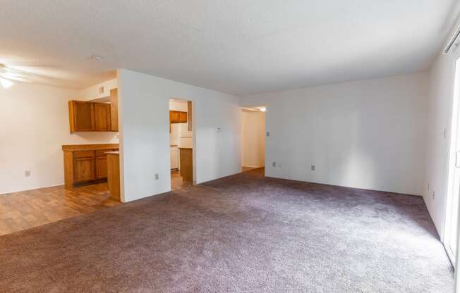 the living room and kitchen of an empty apartment with carpeting and white walls