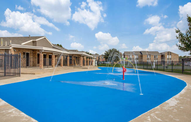 Apartments In Fort Worth, TX - Monarch Pass - Gated Splash Park with Apartment Buildings in the Background.