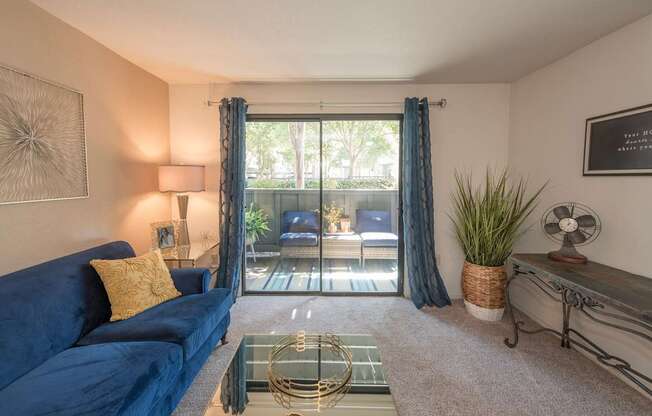 A living room with a blue couch and a glass coffee table at Bishop's Court Apartments, California, 95670