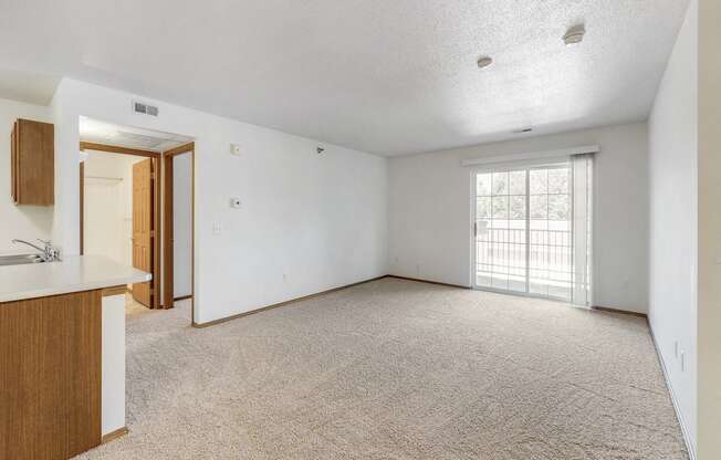 an empty living room and kitchen with a door to a balcony