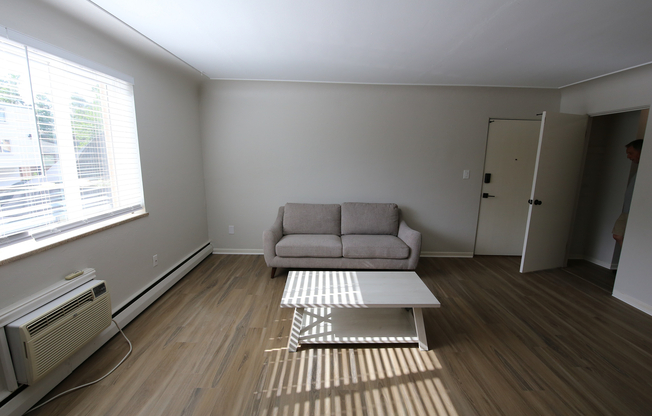 Bright and inviting living area featuring sleek wooden floors, a stylish grey sofa, and a modern coffee table, accented by natural light streaming through large windows.