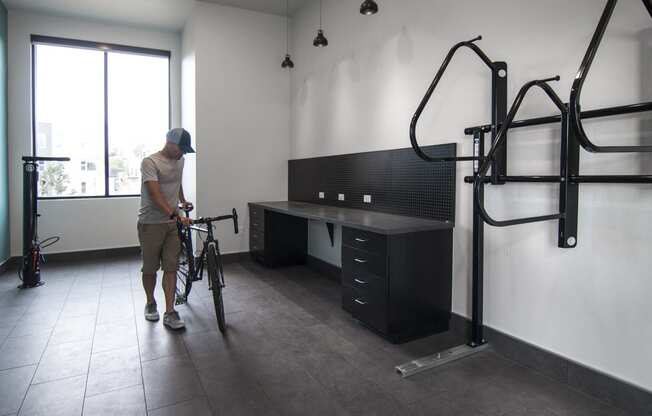 a man is holding a bike in a room with a desk and a bike rack