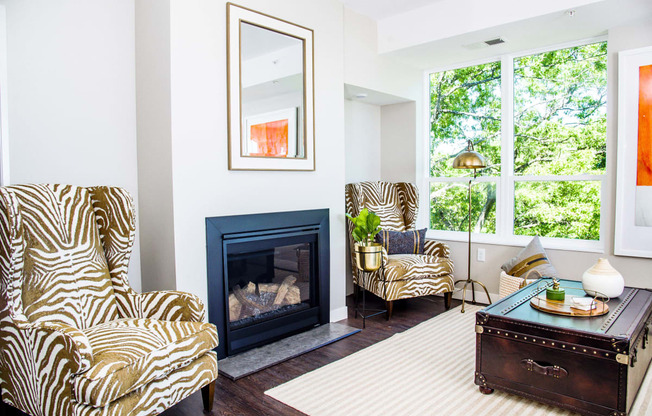 An elegant living room with luxurious stain-resistant plank flooring, a gas fireplace, and expansive windows that offer picturesque views of nature. A seamless transition to a balcony creates a spacious indoor-outdoor connection.