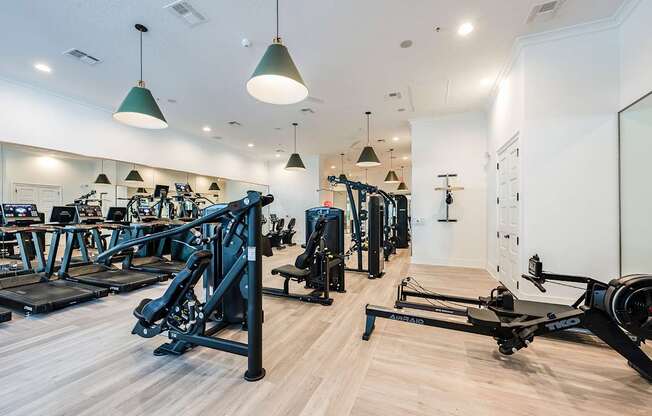 A gym with a variety of equipment including treadmills, rowing machines, and weights.
