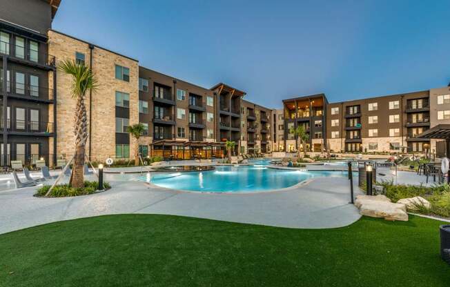 A swimming pool surrounded by a grassy area and apartment buildings.