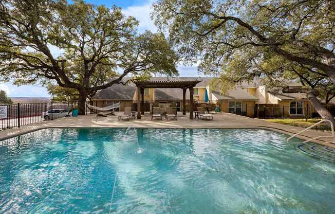 A swimming pool surrounded by trees and a gazebo.