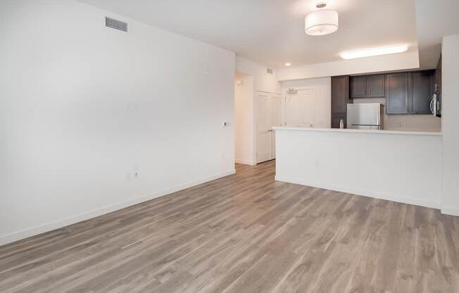 an empty living room with a kitchen in the background