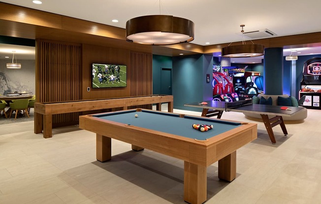 A pool table is in the middle of a room with a TV and a bar.