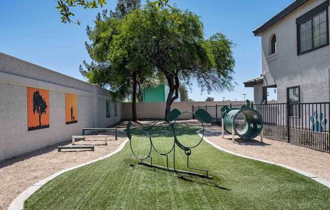 A playground with a swing set and a tree in the middle of a grassy area. at Lazo Apartment Homes, Chandler Arizona