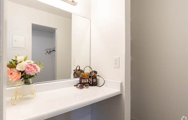 A white bathroom vanity with a mirror, a vase with flowers, a bicycle, and a pair of sunglasses.