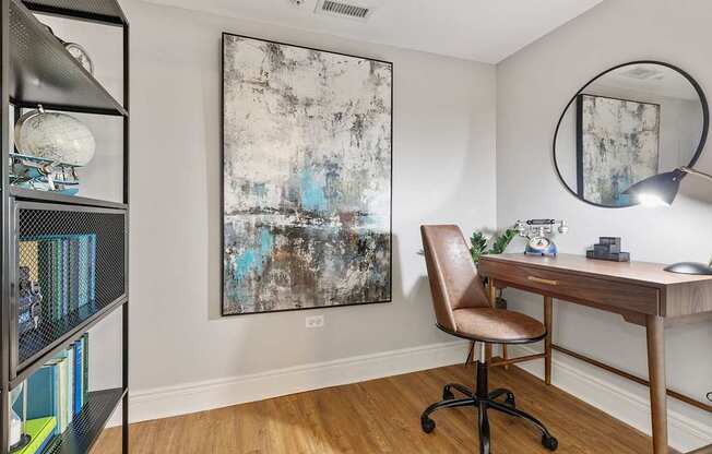 A room with a desk, chair, and a painting on the wall.