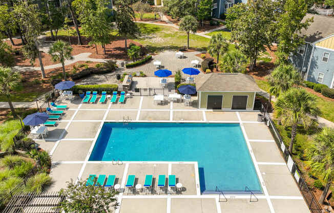 a swimming pool with chairs and umbrellas in front of a house