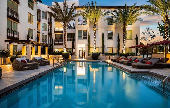 Twilight poolside view with glowing water, lush landscaping, and stylish lounge seating for relaxation