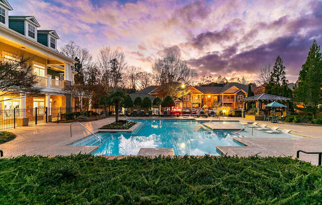 A large outdoor swimming pool surrounded by a grassy area and residential houses.