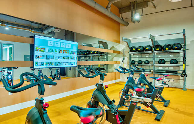 A gym with exercise bikes and a screen showing a workout routine.