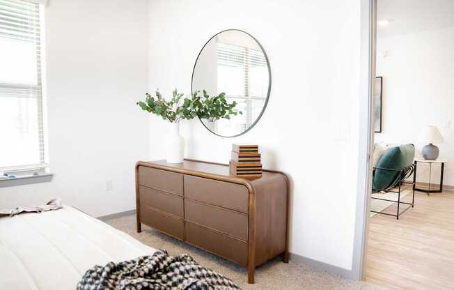 A round mirror hangs on a wall above a wooden chest of drawers.