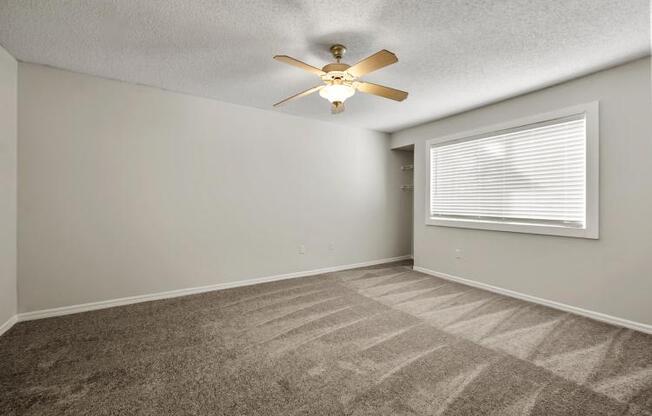 an empty bedroom with a ceiling fan and a window