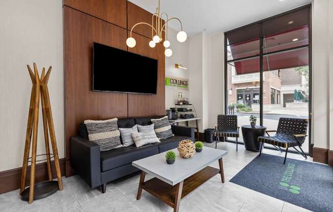 A modern living room with a black couch, a wooden floor, and a flat-screen TV mounted on the wall.