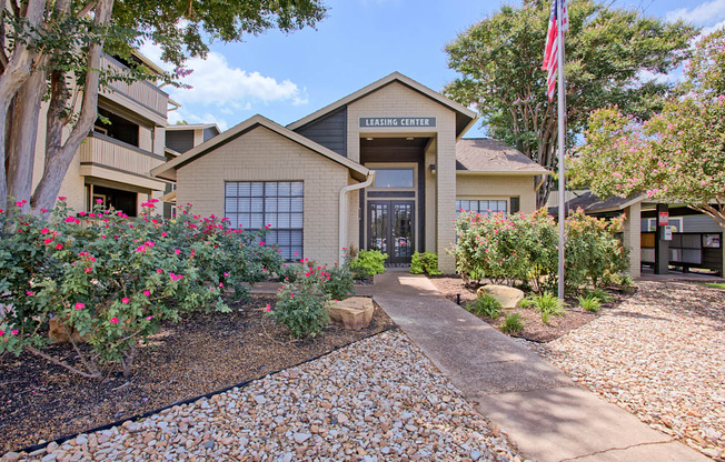 A building with a sign that says "Leasing Center" is surrounded by trees and flowers.