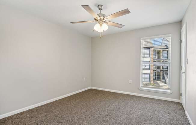 an empty living room with a ceiling fan and a window