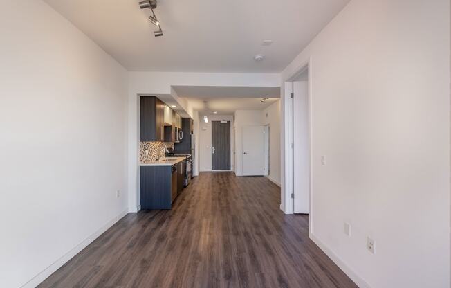 a living room and kitchen with white walls and wood flooring