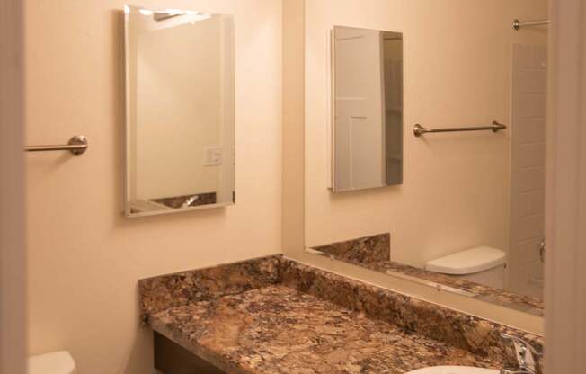 A bathroom with a granite counter top and a mirror with lights above it.