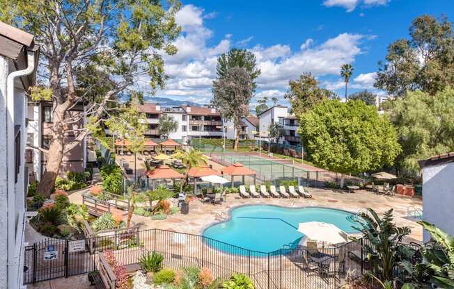 Fusion Warner Center apartments pool surrounded by black iron safety fencing next to tennis courts and courtyard with cabanas and lounge chairs.