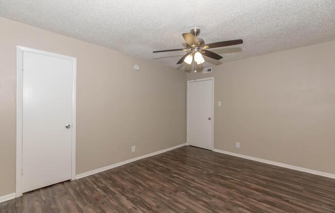 A small, light-colored room with a textured ceiling and a ceiling fan. The walls are painted beige, and there are two white doorsâone visible on the left and the other on the right. The floor is wooden laminate, giving the space a clean and modern appearance.