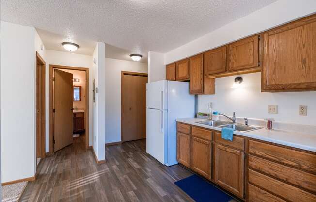 a kitchen with wooden cabinets and a white refrigerator and a door. Grand Forks, ND Chandler 1866 Apartments