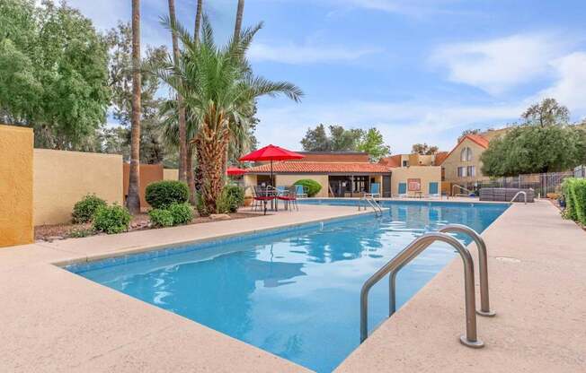 A pool surrounded by palm trees and a red roofed building.