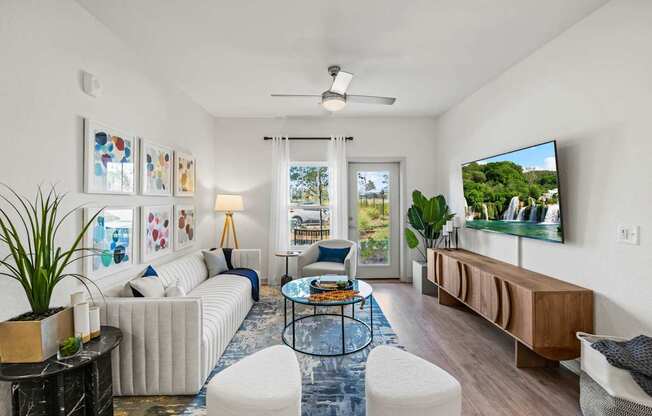 A living room with a white couch, a glass coffee table, and a television on the wall.