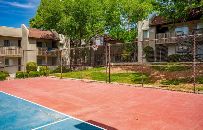 A red and blue basketball court in front of apartment buildings.